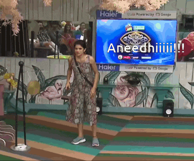 a woman stands in front of a tv screen that says aneediiii