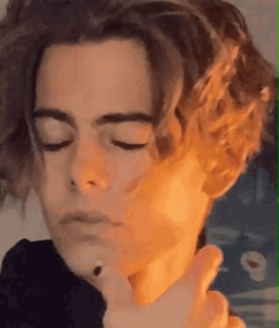 a close up of a young man 's face with his eyes closed and his hand on his chin .