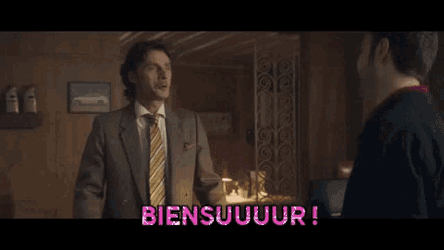 a man in a suit and tie is talking to another man in a room with the word biensuuuur written in pink