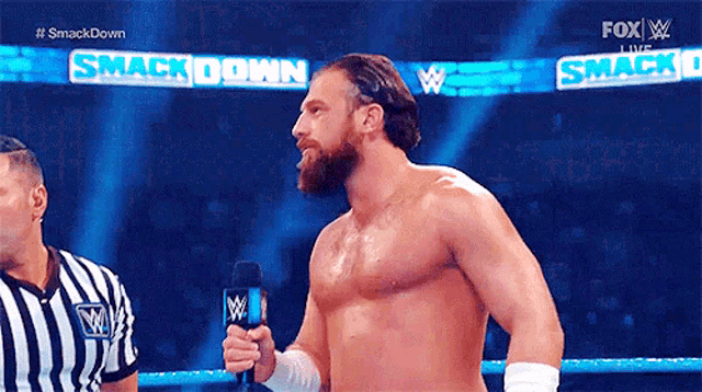 a shirtless wrestler is talking into a microphone while standing in a wrestling ring .