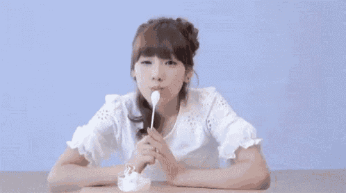 a young woman is sitting at a table with a bowl of ice cream in her hand .