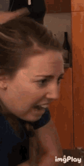 a woman is making a funny face in a kitchen with a bottle of wine behind her .