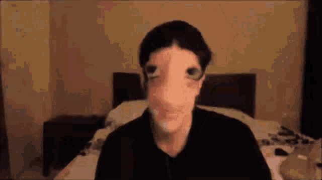 a man with a big nose is sitting on a bed in a bedroom .