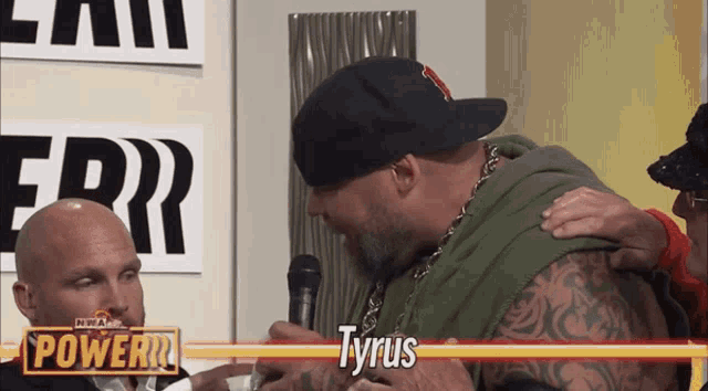 a man named tyrus is talking to another man in front of a microphone