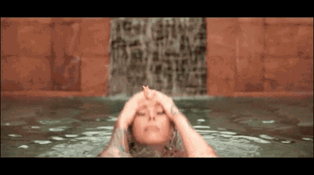 a woman is swimming in a pool with a waterfall behind her