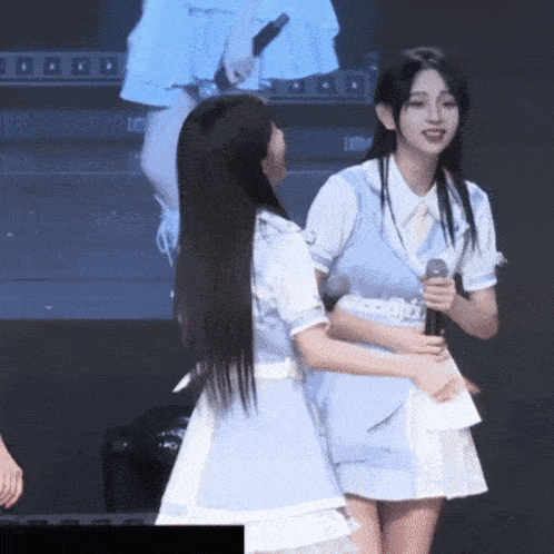 a girl in a blue dress holds a microphone while standing next to another girl