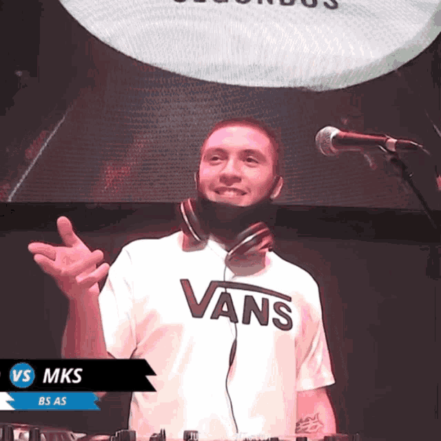 a man wearing headphones and a vans shirt is standing in front of a microphone