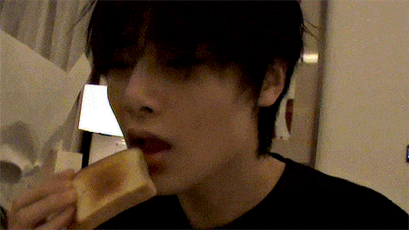 a young man is eating a piece of bread in a dark room