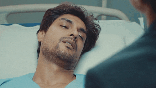 a man laying in a hospital bed talking to another man