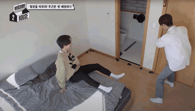 two men are sitting on a bed with a sign that says welcome 2 house on it