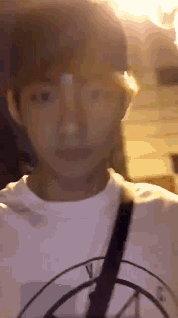 a man wearing a white shirt with a circle on it looks at the camera