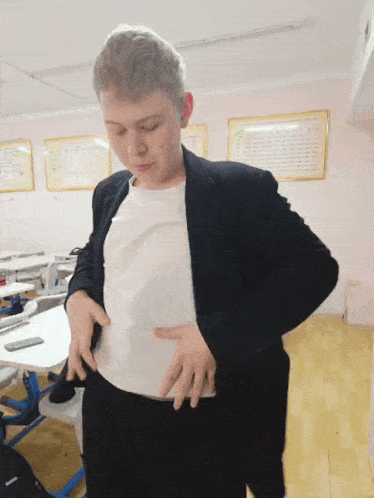 a boy in a suit and white shirt is standing in a classroom