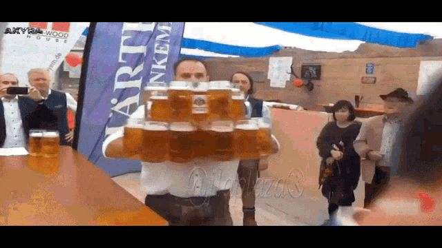 a man is holding a stack of beer glasses in front of a banner that says artt