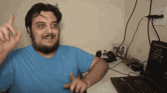 a man in a blue shirt sitting in front of a laptop computer