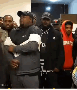 a group of men are standing in a room and one of them is wearing a hoodie that says tnfsdz