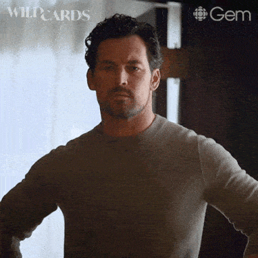 a man in a grey sweater is standing with his hands on his hips in front of a sign that says wildcards