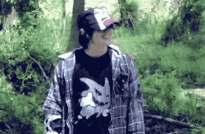 a man wearing a hat and a plaid shirt is walking through the woods .