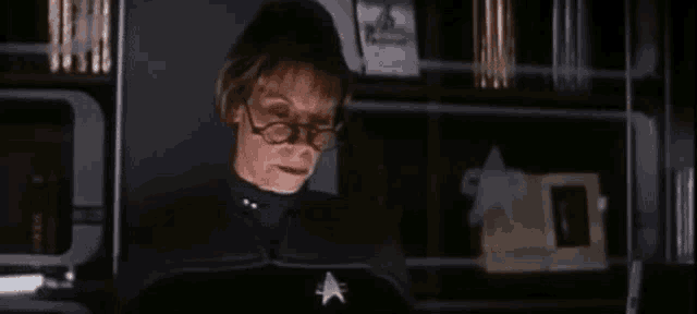 a woman wearing glasses and a star trek uniform is sitting in a dark room .
