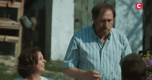 a man in a blue striped shirt stands next to a woman in a white shirt with a red c on the bottom right