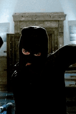 a man wearing a black ski mask stands in a dark room