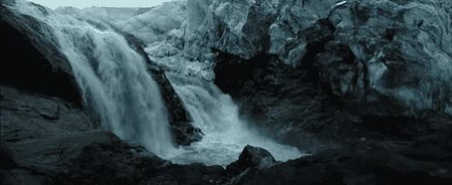 a waterfall in the middle of a cave surrounded by rocks and ice .