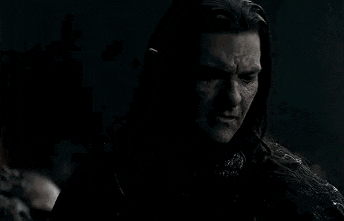 a man with long hair is standing in the dark with a sword in his hand .