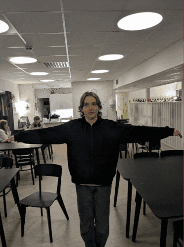 a man with his arms outstretched stands in a room with chairs and tables