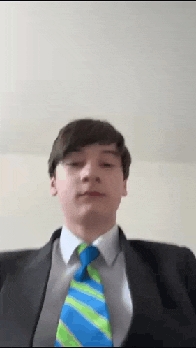 a young man in a suit and tie looks at the camera