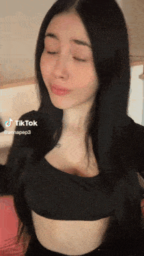 a woman with long black hair is wearing a black crop top and has a tattoo on her chest ..