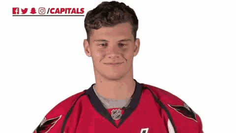 a hockey player is waving his hand and smiling while wearing a red jersey .