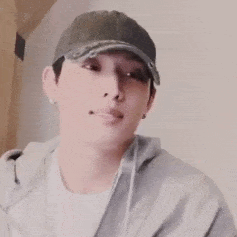 a man wearing a baseball cap and a gray hoodie is making a funny face .