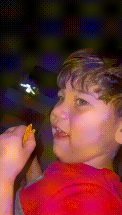 a young boy in a red shirt is eating a chip