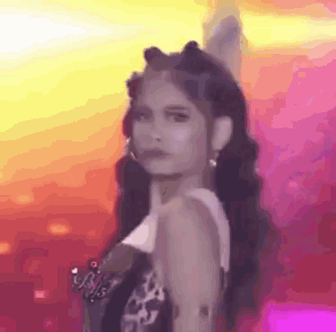 a woman with long hair is standing in front of a pink background and looking at the camera .