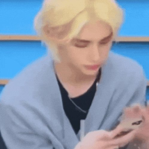 a man with blonde hair is holding a cell phone in his hand .
