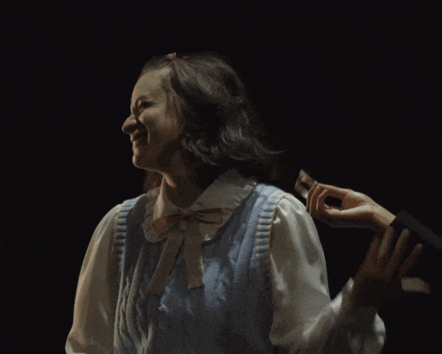 a woman in a blue vest is laughing while a man holds her hair