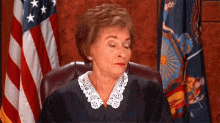a judge is sitting in front of an american flag with her eyes closed