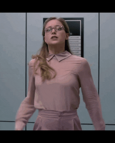 a woman wearing glasses and a pink shirt is standing in front of a sign that says ' a '