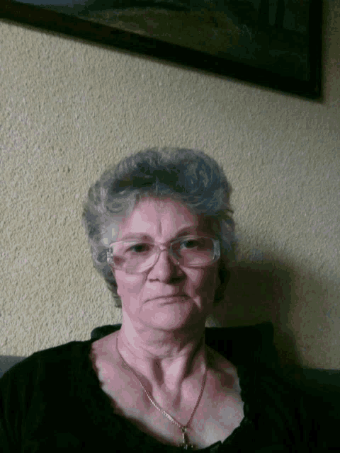 an older woman wearing glasses and a black shirt looks at the camera