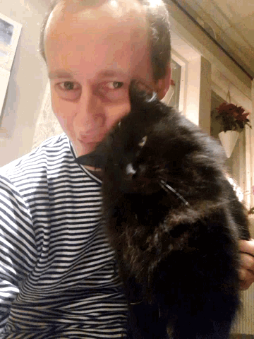 a man in a striped shirt holds a black cat in his lap