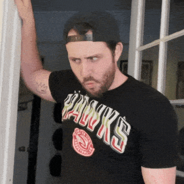 a man wearing a hawks t-shirt is leaning against a door
