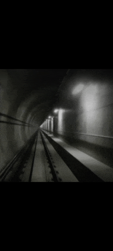 a black and white photo of a train going through a dark tunnel