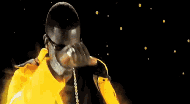 a man in a yellow jacket is covering his face with his hand while standing in front of a black background .