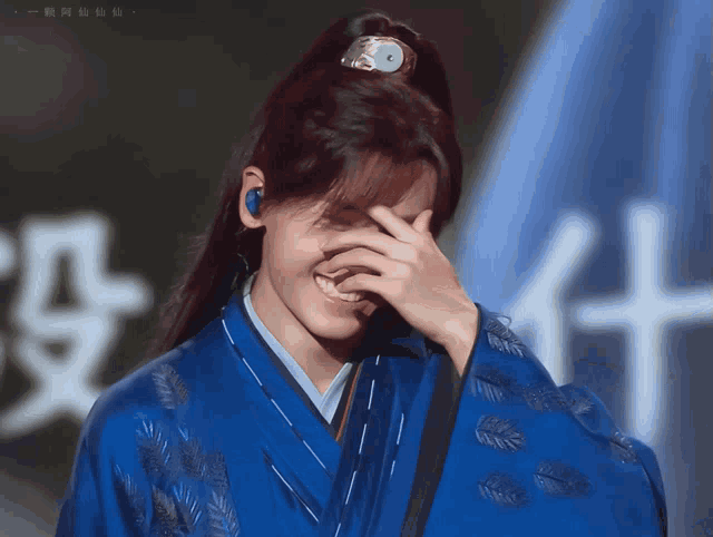 a person wearing a blue kimono covering their face with their hand