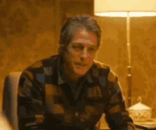 a man in a plaid shirt is sitting in front of a lamp in a room .