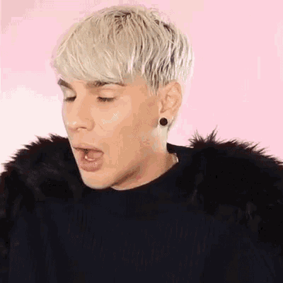 a man with blonde hair and earrings is wearing a black fur coat .