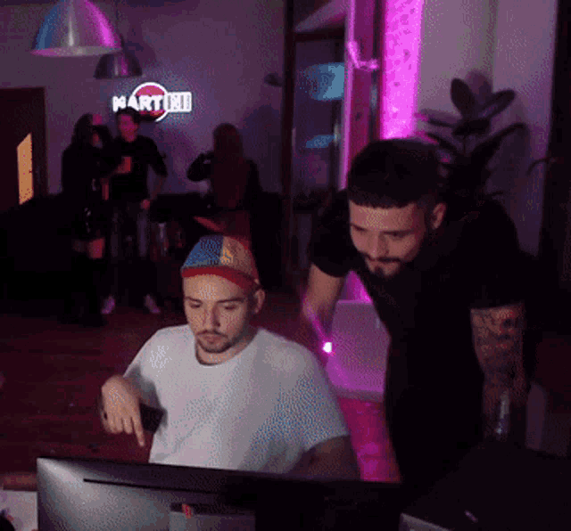 two men are looking at a computer screen with a martini sign in the background