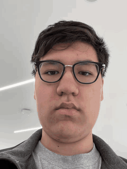 a young man wearing glasses looks at the camera with a serious look on his face