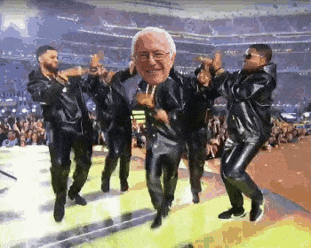 a group of men are dancing on a stage with a picture of bernie sanders in the middle of the picture .