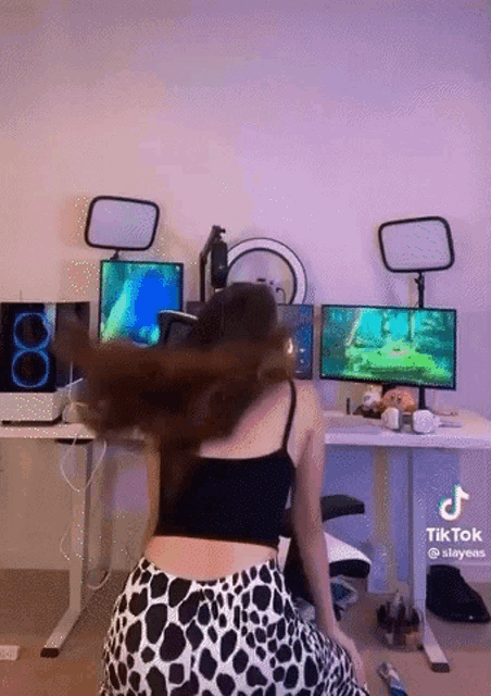 a woman in a cow print skirt is sitting in front of a desk with two computer monitors .