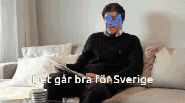 a man sits on a couch reading a newspaper with a blue letter m on his face